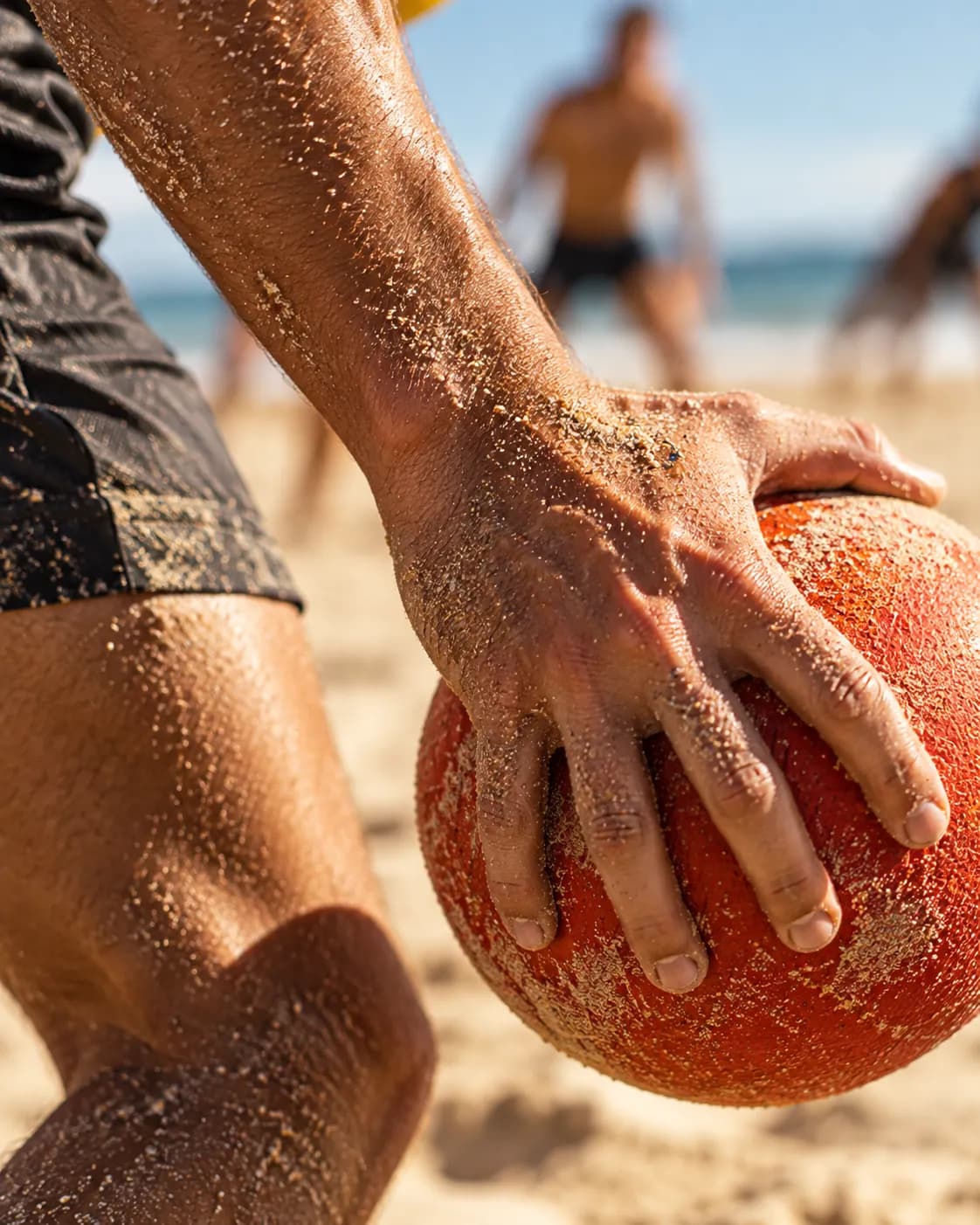 Primer plano de una mano cubierta de arena que sujeta un balón naranja