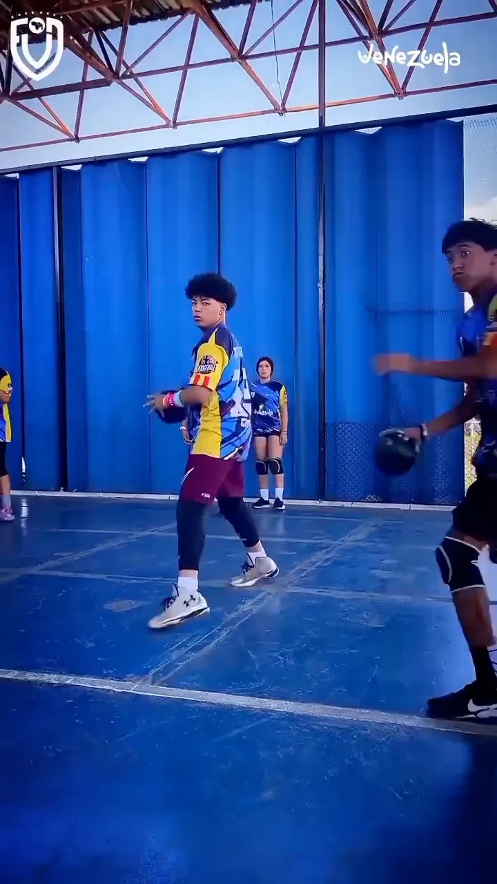 Dos jugadores de la selección se enfrentan con el balón en la mano en una cancha techada de piso azul