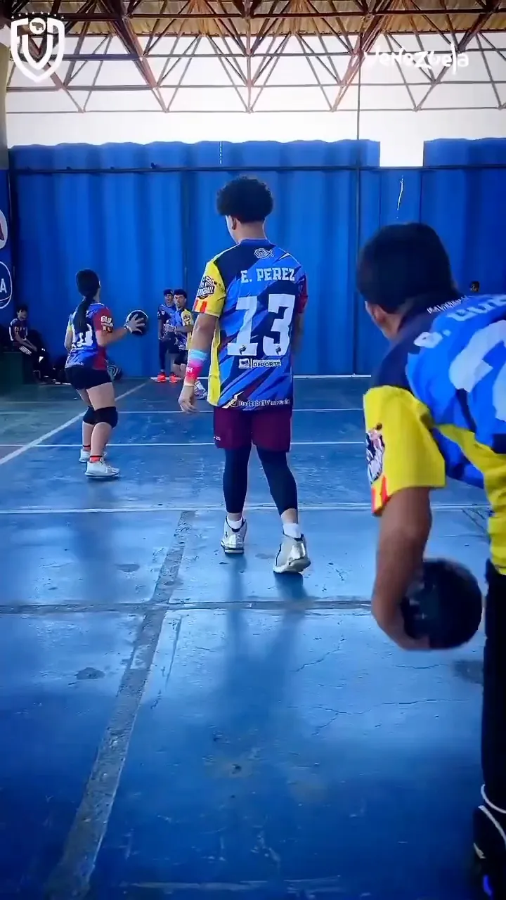 Jugadores de la selección en plena práctica, vistos de espaldas, con balones en juego y cortinas azules al fondo