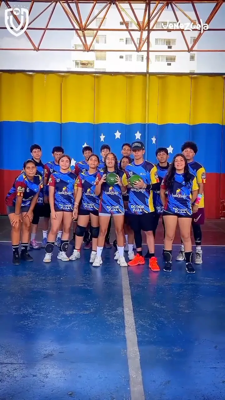 La Selección Venezolana de Dodgeball posa en grupo en una cancha techada, frente a una gran bandera de Venezuela